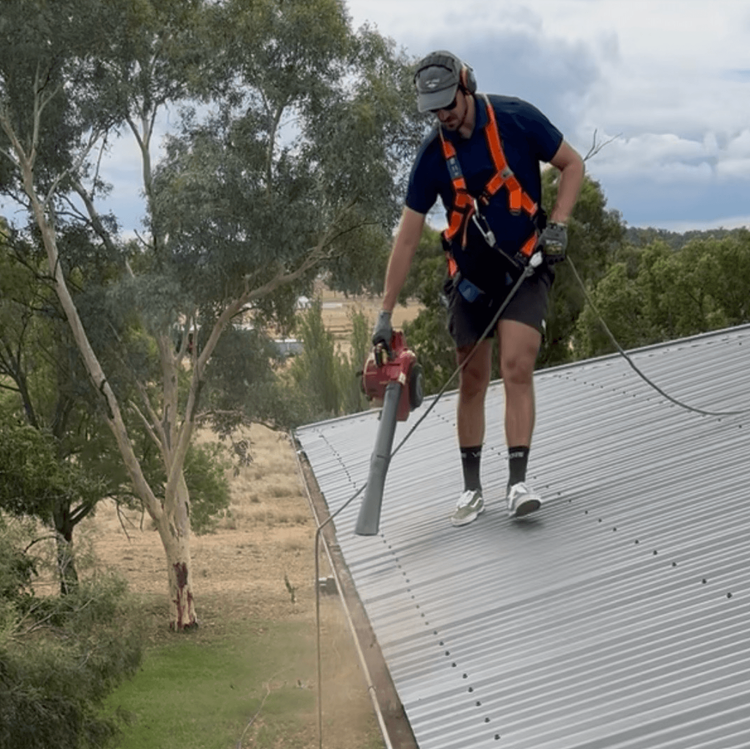 A professional technician using a leaf blower to clean a gutter.